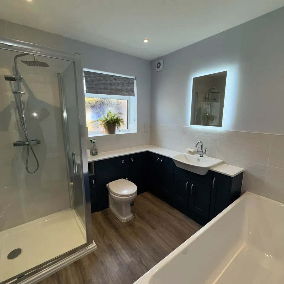 A bathroom with a glass shower, bath and navy vanity unit, cleaned and shining